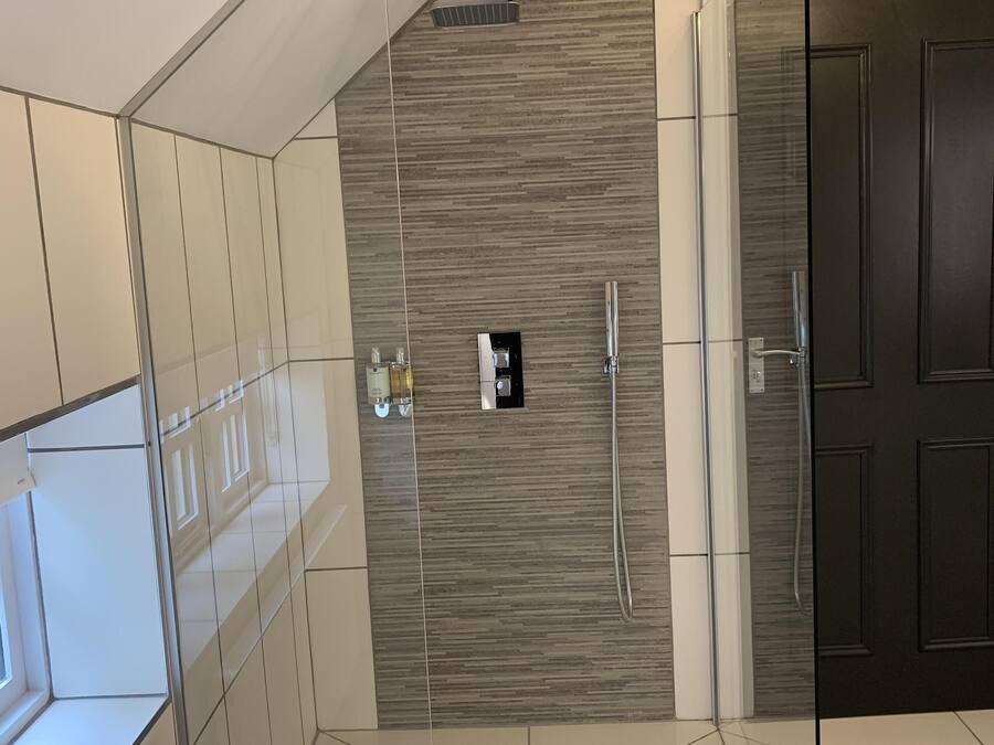 A modern bathroom with a glass shower enclosure, a towel rack, and a dark wooden door.
