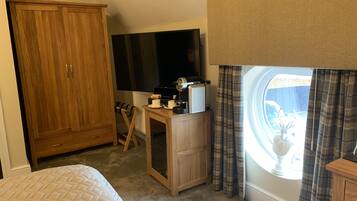 A bedroom with a bed, a wooden wardrobe, a desk with a radiator, a television, and a window with curtains.