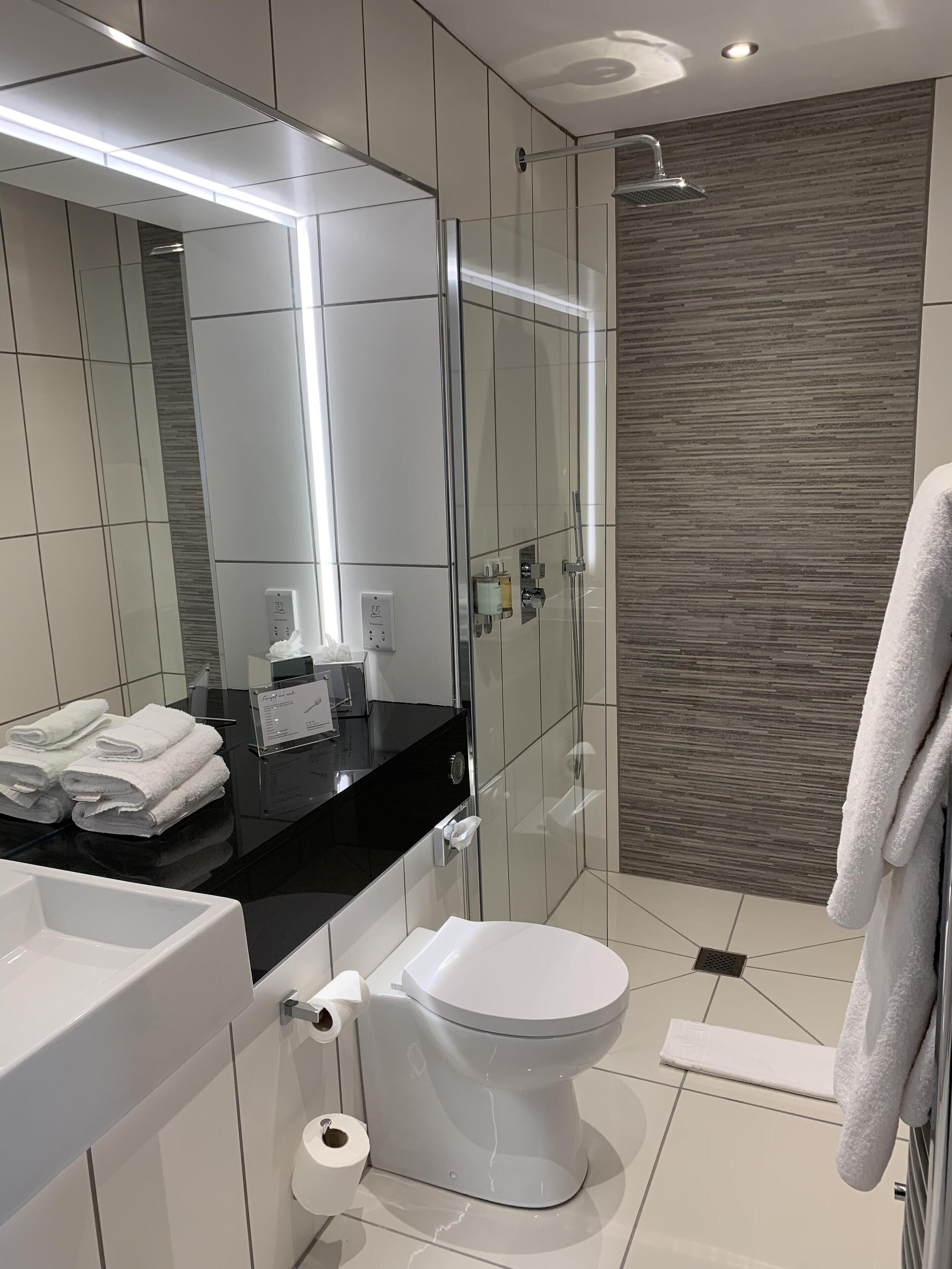 A modern bathroom with a large mirror, a black countertop, a white toilet, and a shower area.
