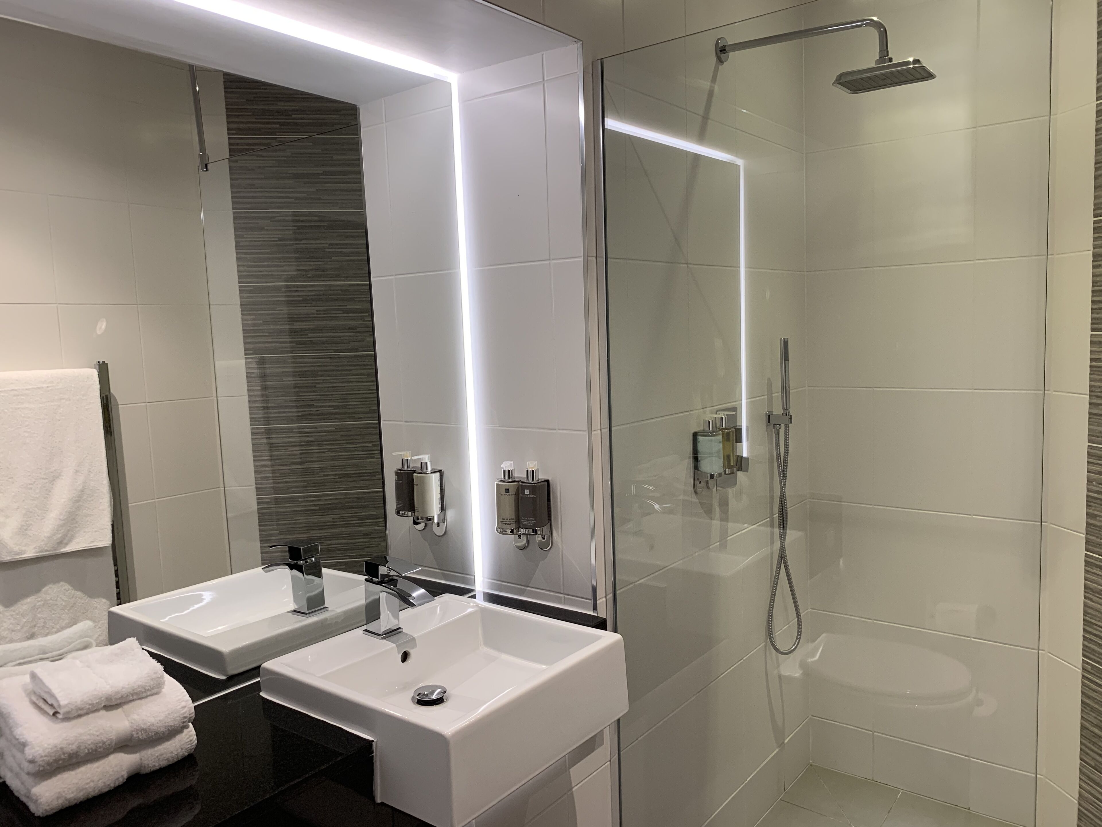 A modern bathroom with two sinks, a glass shower enclosure, and a large mirror.