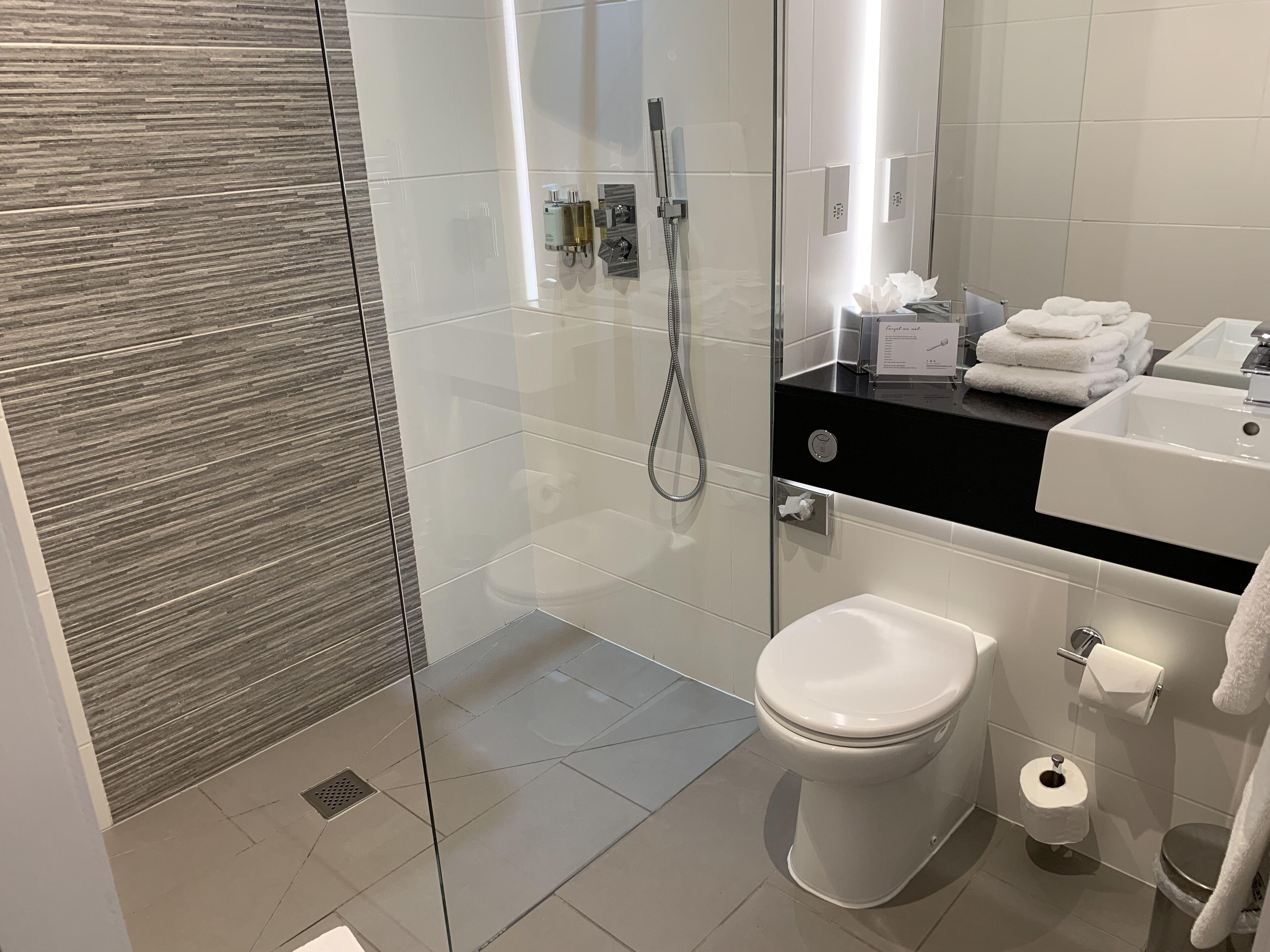 A modern bathroom with a glass-enclosed shower, a toilet, and a sink with a black countertop.