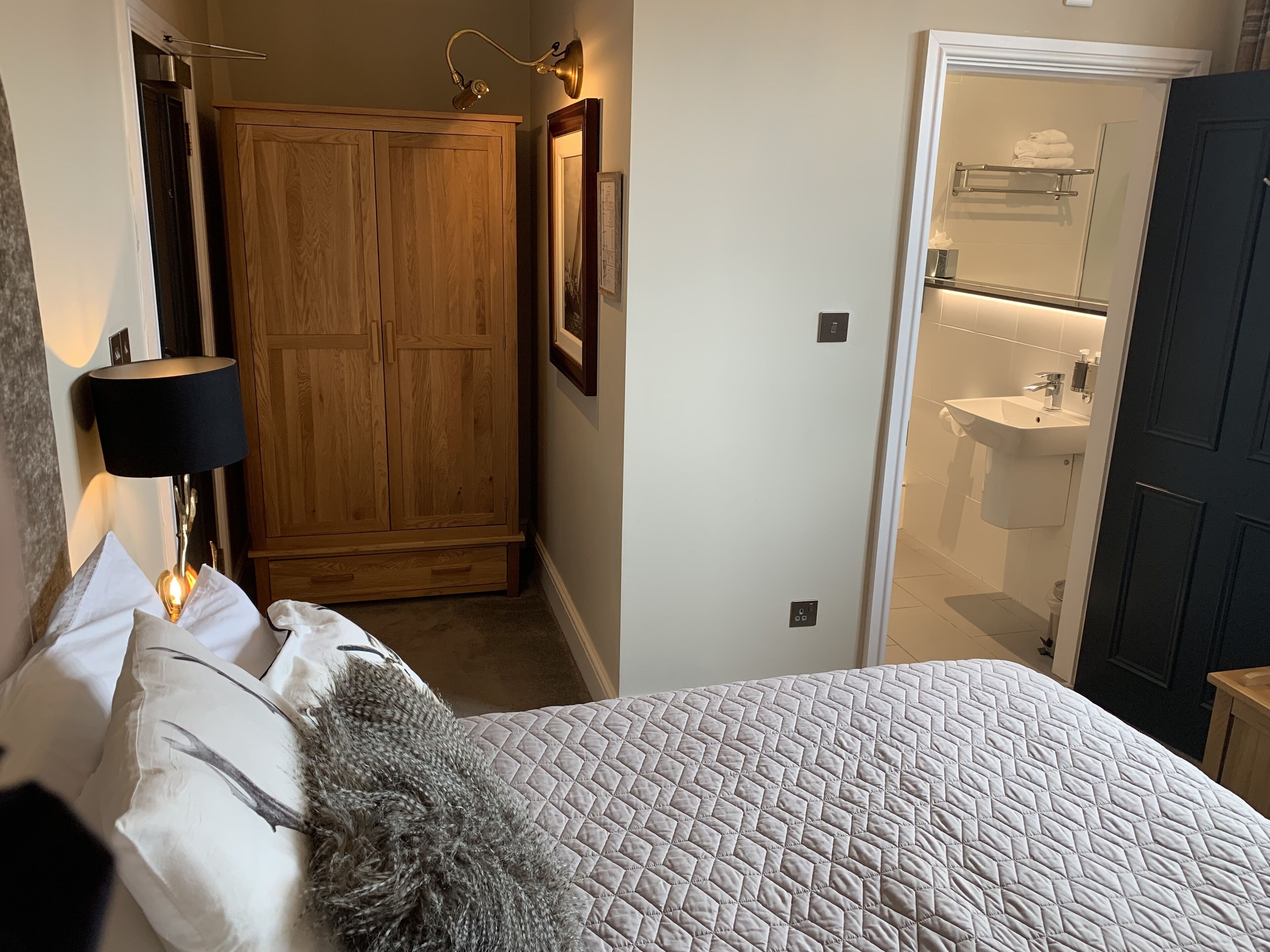 Una camera da letto con un letto, un armadio in legno, un bagno con lavandino e specchio, e una porta che dà su un'altra stanza.