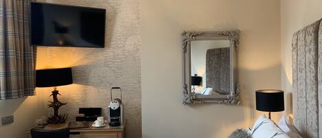 Habitación de hotel con cama, escritorio con computadora, televisor de pantalla plana, cafetera y espejo.