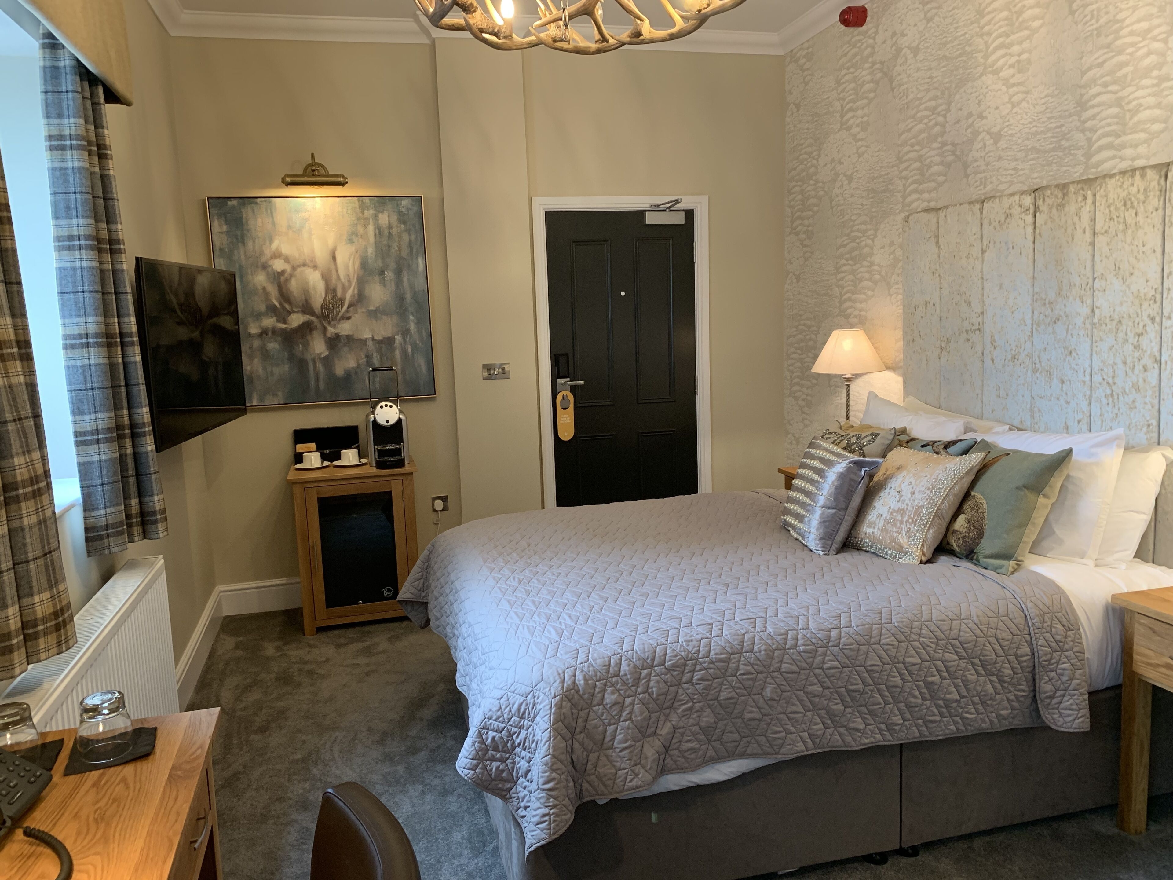 A bedroom with a large bed, a bedside table, a lamp, a painting, and a door.