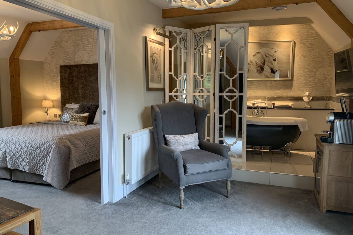 A bedroom with a bed, a chair, a radiator, a mirror, and a bathroom with a bathtub and sink.