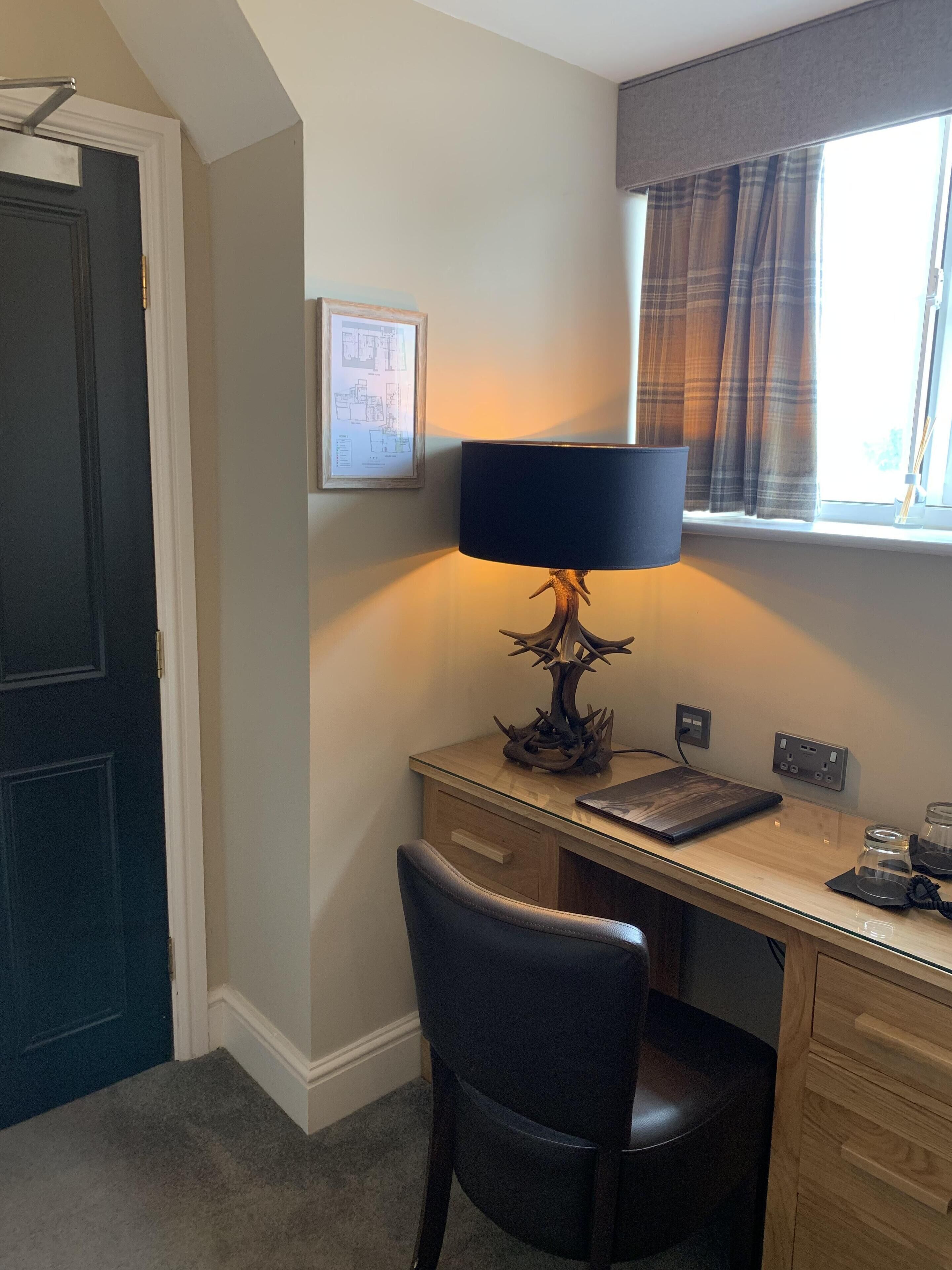 A room with a desk, chair, lamp, and window with curtains.
