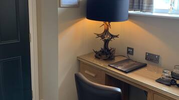 A room with a desk, chair, lamp, and window with curtains.