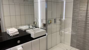 Un baño moderno con dos lavamanos, una cabina de ducha de vidrio y una encimera negra.