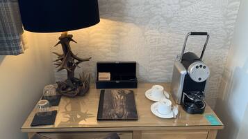 Un escritorio de hotel con una lámpara, una cafetera, un vaso de agua, una taza y una caja de pañuelos.