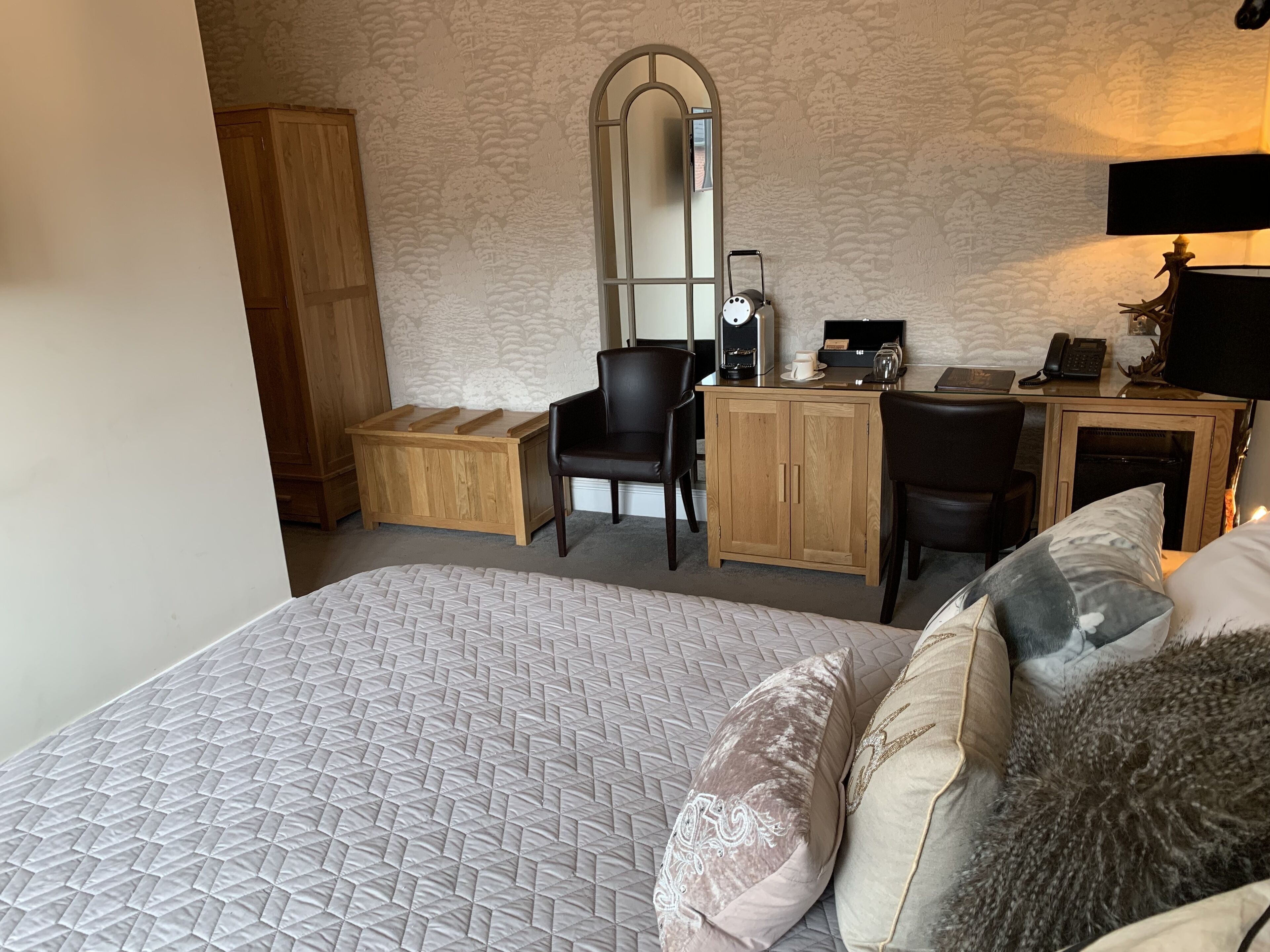 A bedroom with a large bed, a desk, a chair, a wardrobe, and a mirror.