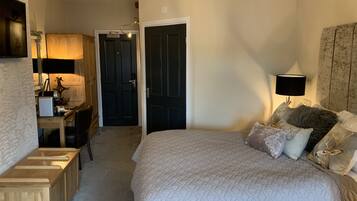 A bedroom with a large bed, a desk, a chair, a lamp, and a door.