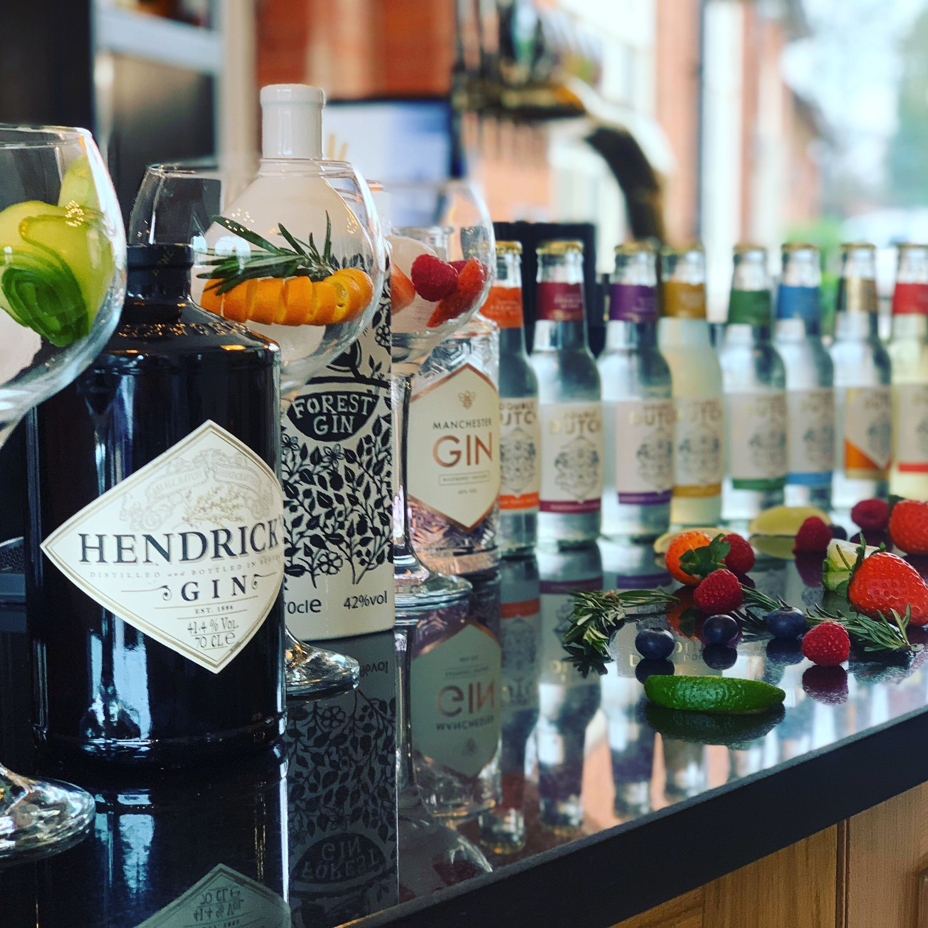 A bar counter with various bottles of gin and other beverages, garnished with fruits and herbs.