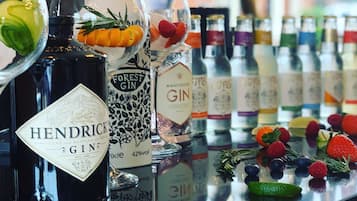 A bar counter with various bottles of gin and other beverages, garnished with fruits and herbs.