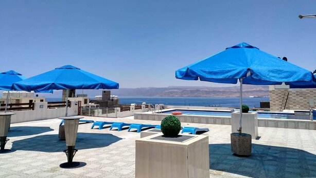 A rooftop terrace with blue umbrellas, lounge chairs, and a pool. - Mass Paradise Hotel (Aqaba)