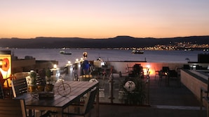 An outdoor terrace with tables and chairs, overlooking a body of water with boats and a cityscape in the distance. - Mass Paradise Hotel (Aqaba)