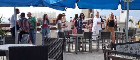 An outdoor seating area with tables and chairs under blue umbrellas, overlooking a cityscape.