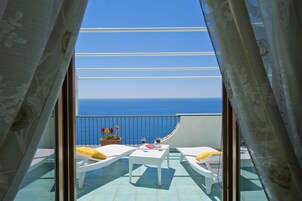 Un balcón con vista al mar, muebles de mimbre blancos y una mesa con bebidas y un libro.