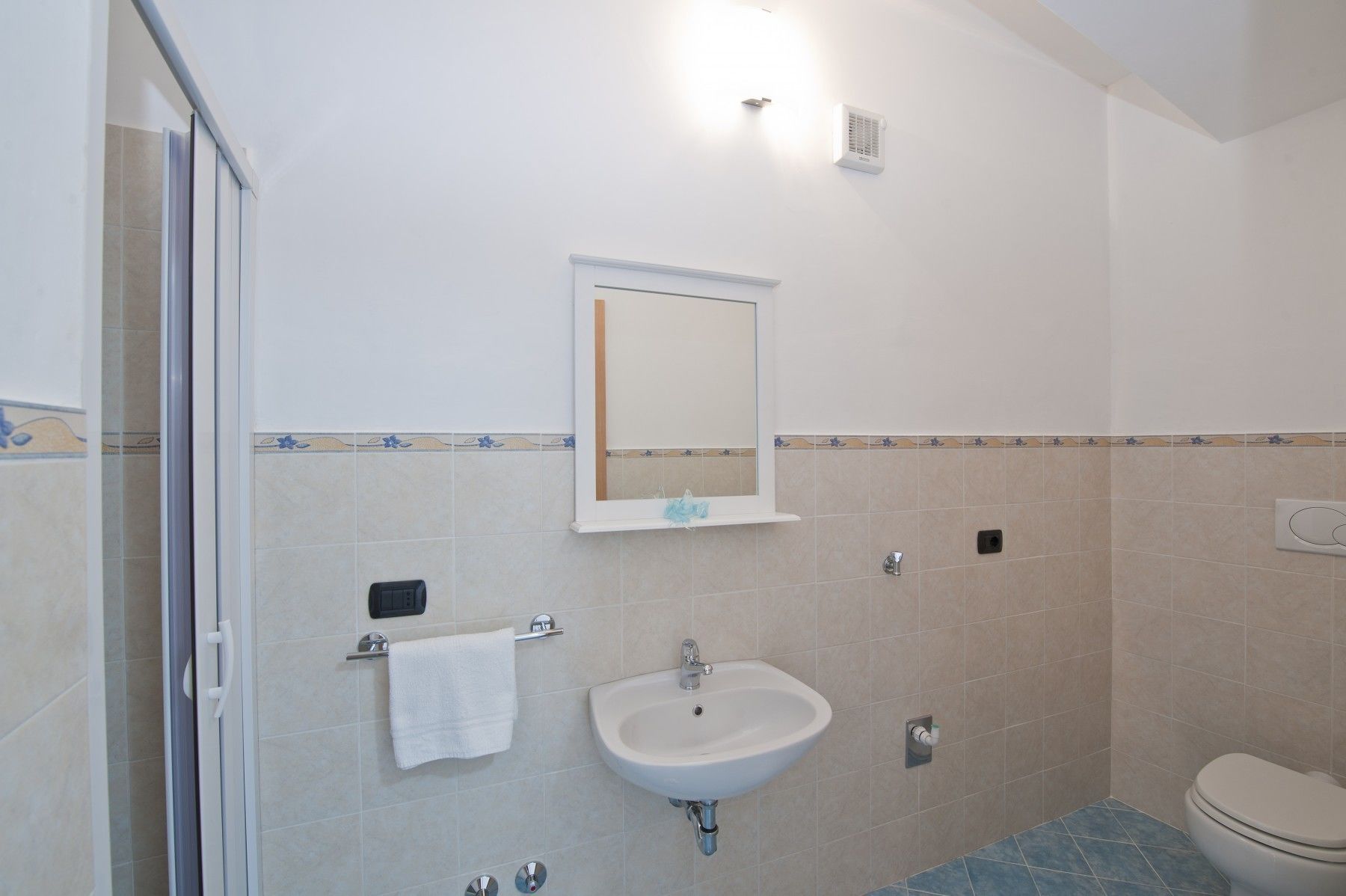 A bathroom with a shower, sink, toilet, and a mirror.