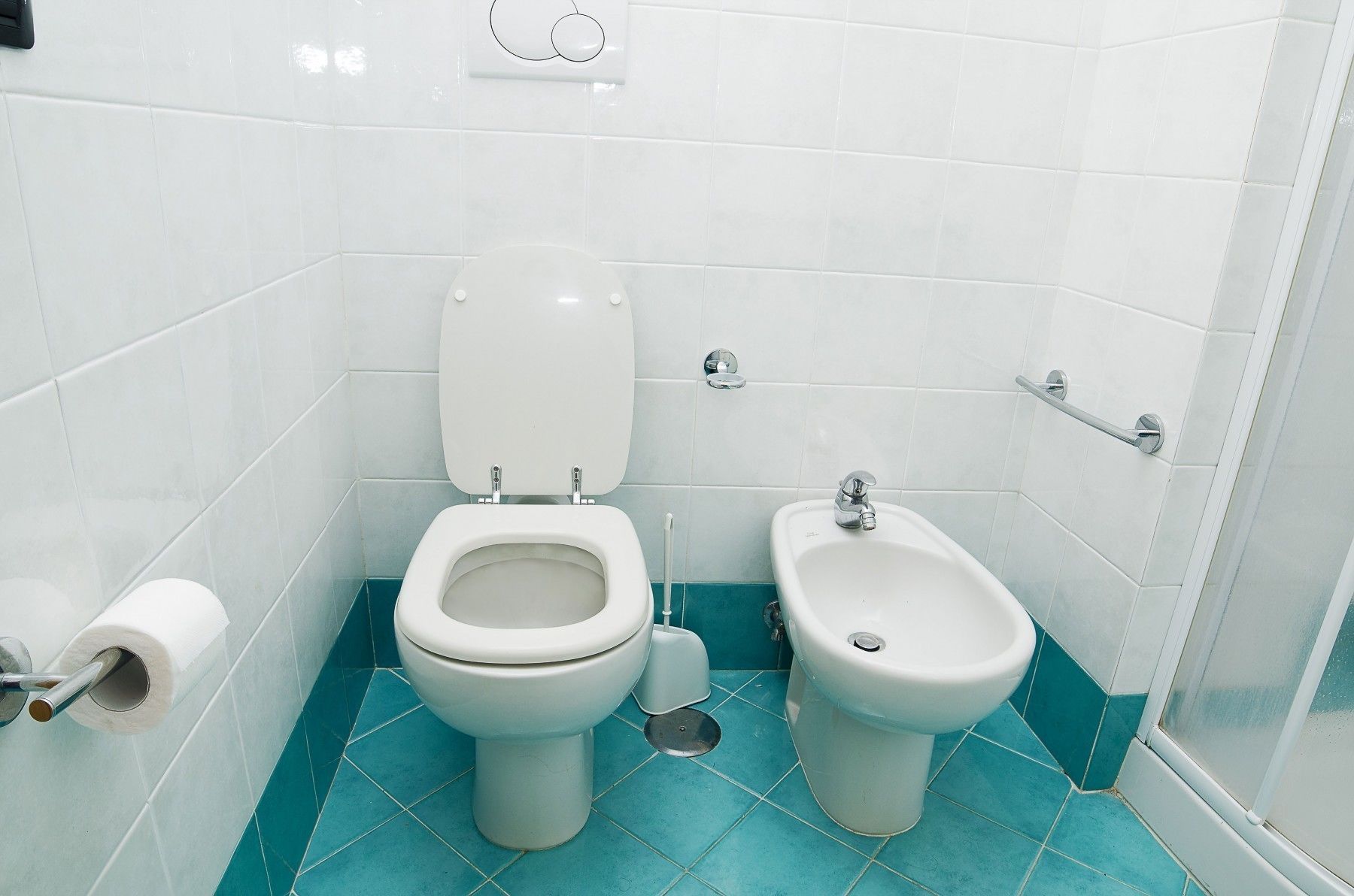 A bathroom with a toilet, bidet, and a toilet paper holder.