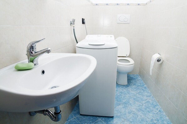 Un baño con lavamanos, inodoro y lavadora.