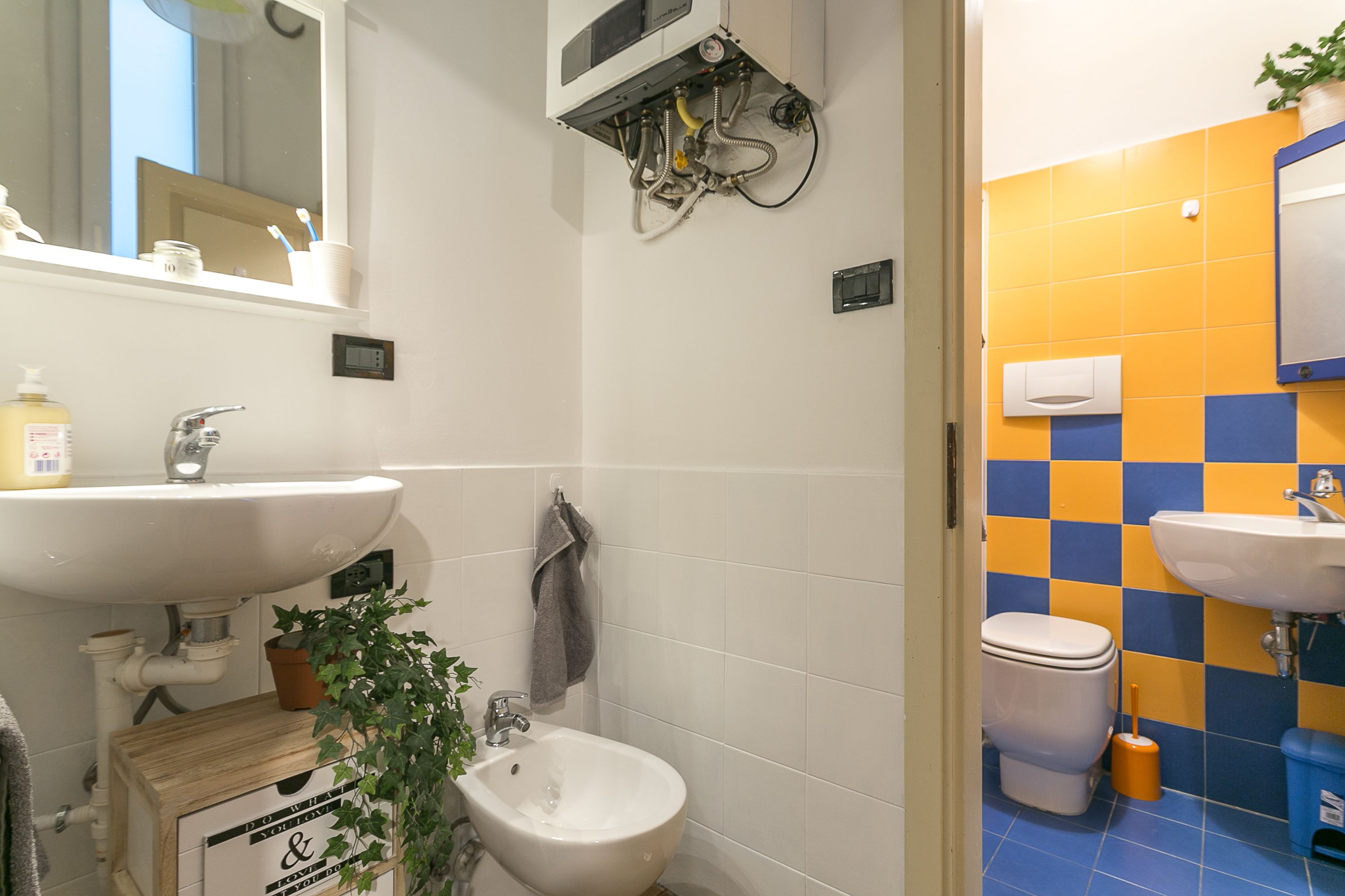 Ein Badezimmer mit zwei Waschbecken, einer Toilette und einem Bidet. Über dem Waschbecken hängt ein Spiegel, und ein Handtuchhalter ist zu sehen.