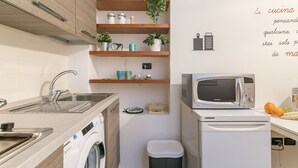 A compact kitchen with a washing machine, microwave, and wooden shelves with plants. - notaMi -  Borsieri 29 (Milan)