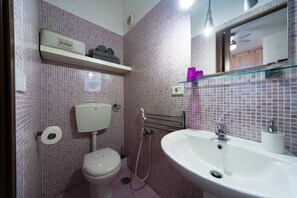 A bathroom with pink mosaic tiles, a toilet, a sink, a shower, and a storage shelf. - Il Sole (Trani)