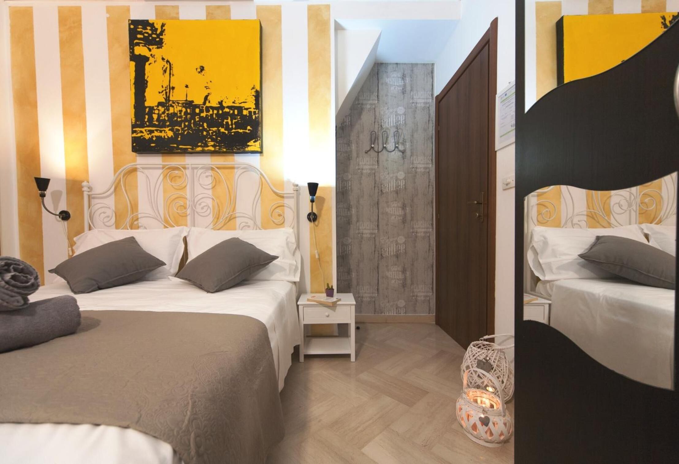 Camera d'albergo con un letto, comodino, lampada e un quadro giallo e nero appeso al muro.