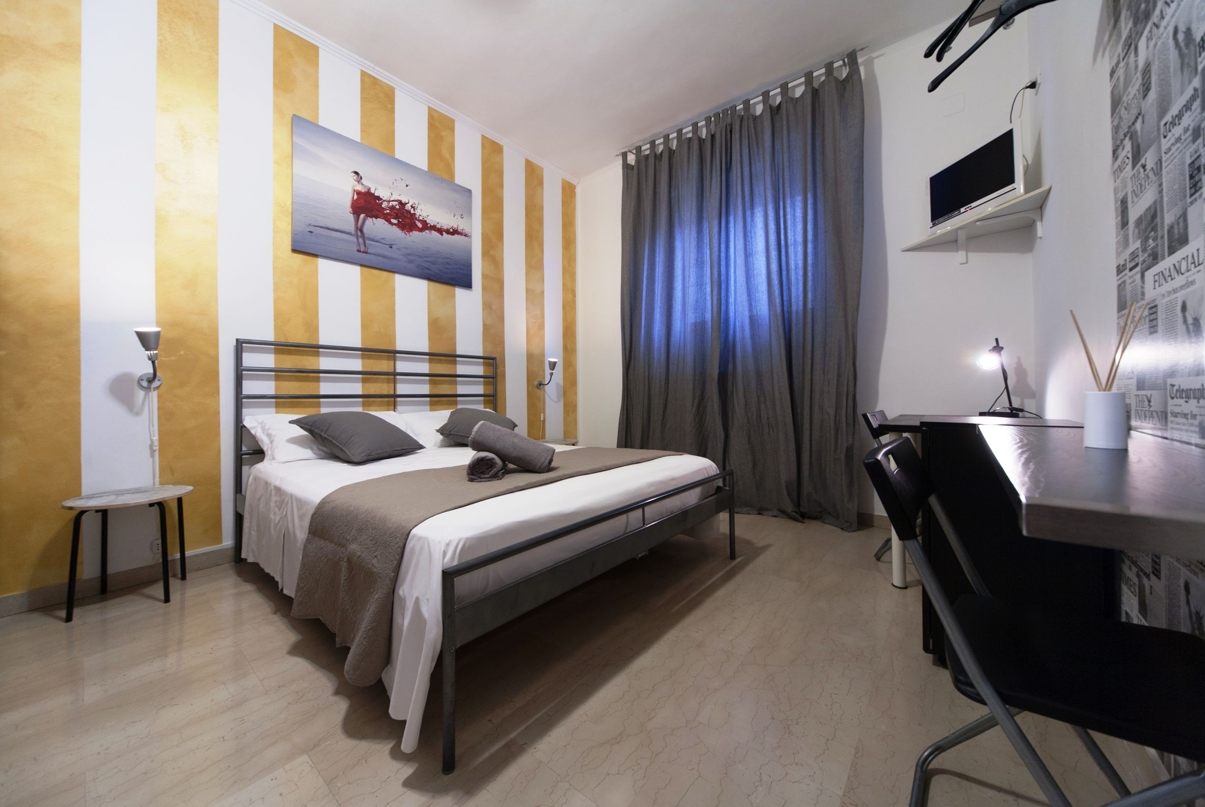 A bedroom with a bed, a desk, a chair, a TV, and a painting on the wall.
