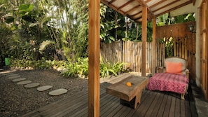 A wooden deck with a bench and a table, surrounded by a bamboo fence and lush greenery. - Villa Desa Roro Estate by Villa Finder (Canggu)