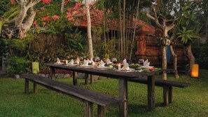 An outdoor dining setup with a wooden table, benches, and candles. - Villa Desa Roro Estate by Villa Finder (Canggu)