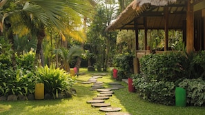A garden with a thatched-roof structure, a stone pathway, and lush greenery. - Villa Desa Roro Estate by Villa Finder (Canggu)