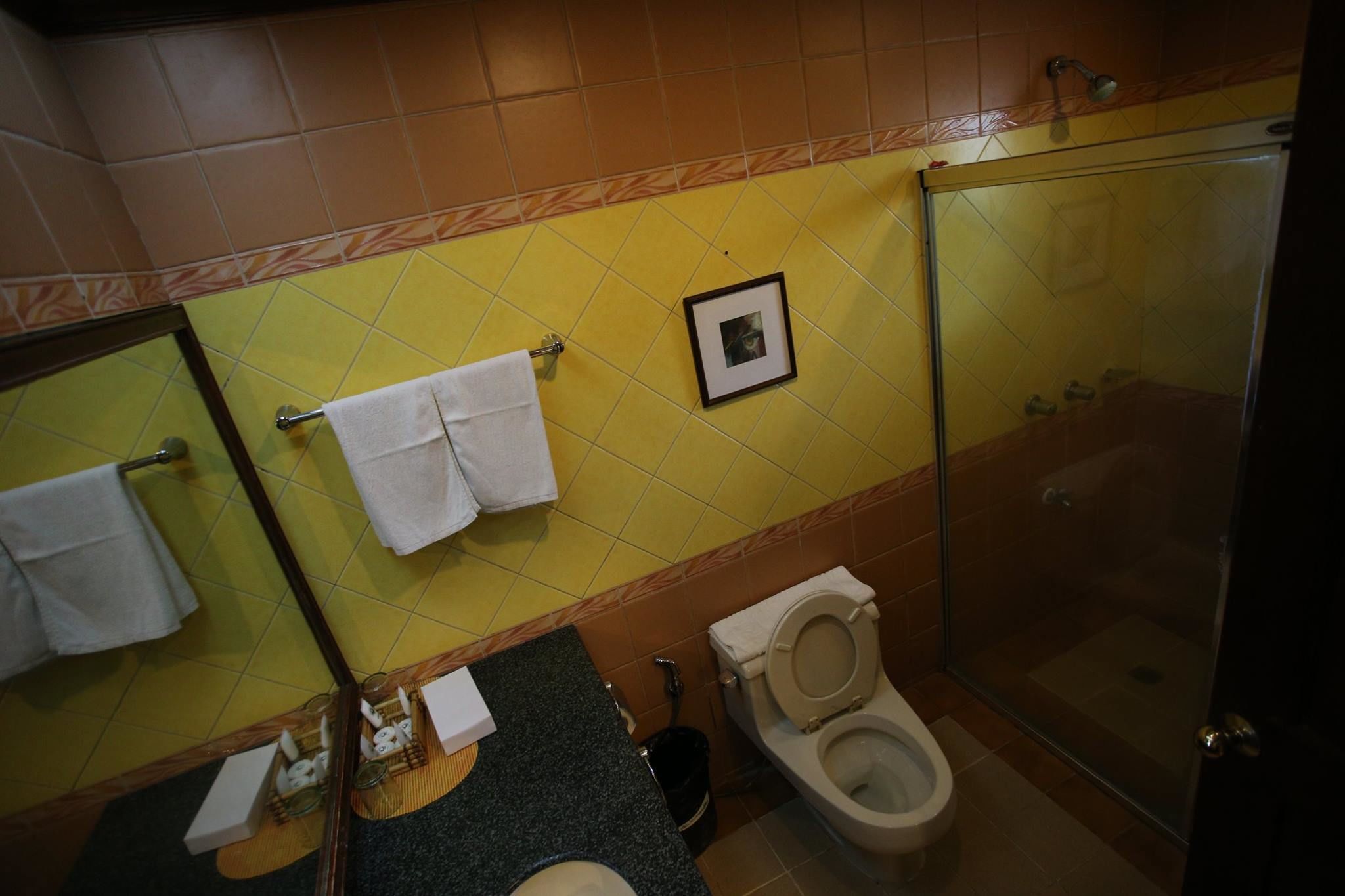 Ein Badezimmer mit gelben und braunen Fliesen, einer Glasdusche, einer Toilette und einem Waschbecken mit Spiegel.