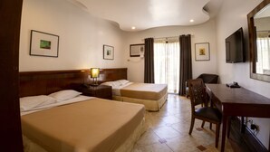 A hotel room with two beds, a desk, a chair, a TV, and a window with curtains.