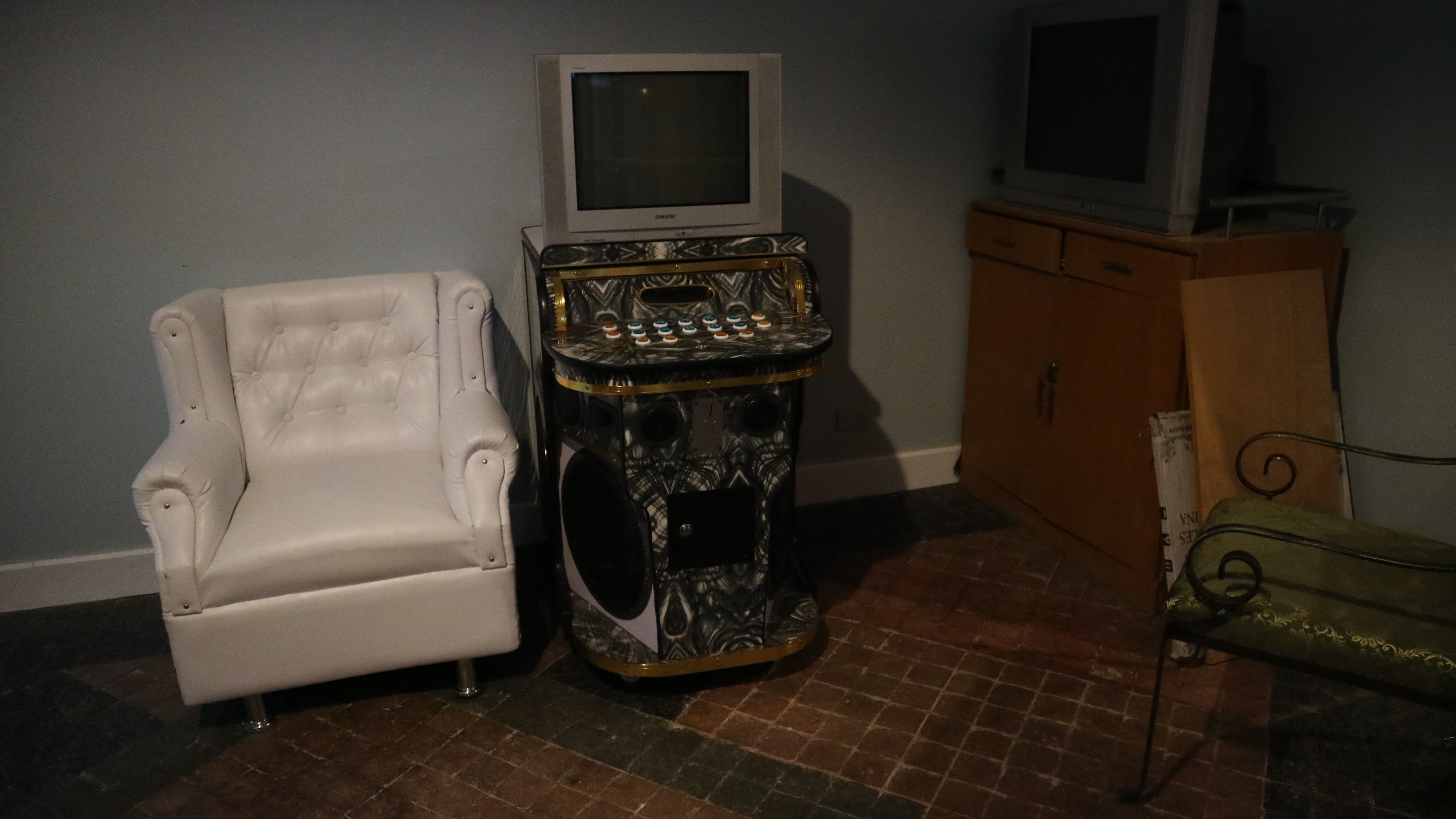 A room with a white armchair, a console table with a television, and a cabinet.