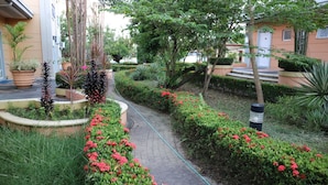 A garden pathway with red flowers and various plants, surrounded by buildings.