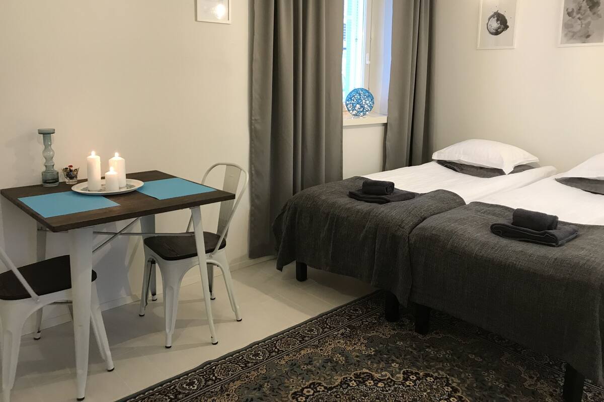 A room with two beds, a desk with a chair, a window with curtains, and a rug.