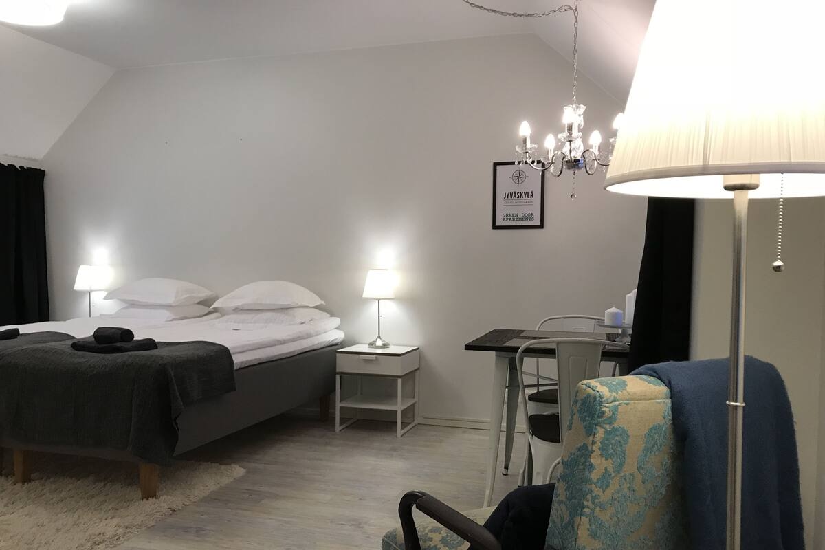 A bedroom with a bed, bedside tables, a desk, a chair, and a chandelier.