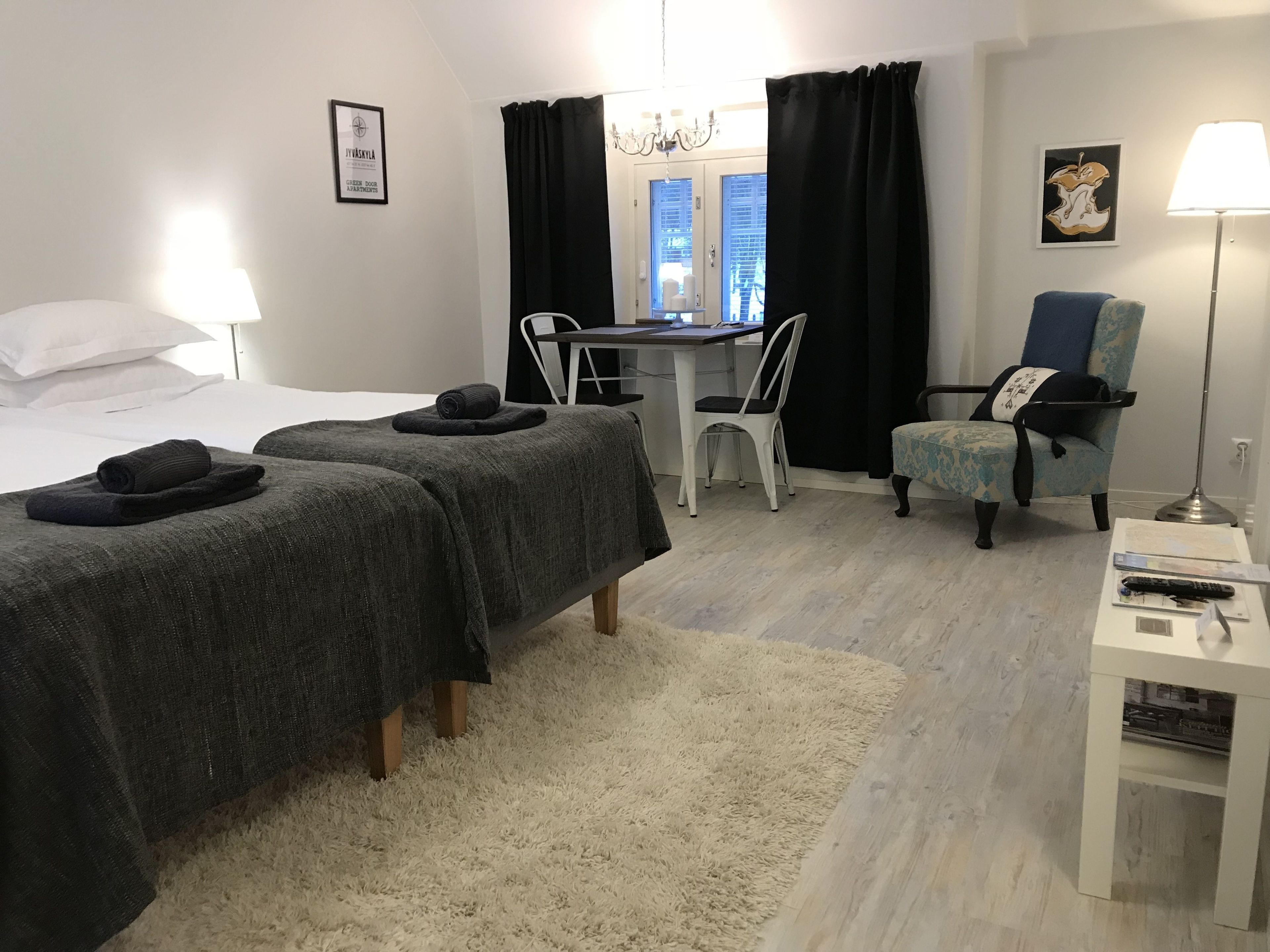 Hotellihuone, jossa on kaksi sänkyä, työpöytä, tuoli, lamppu ja taulu seinällä.