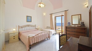 Une chambre à coucher avec un lit, des tables de chevet, une commode, un miroir et une vue sur la mer.
