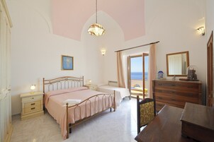 Un dormitorio con cama, mesitas de noche, cómoda, espejo y vista al mar.