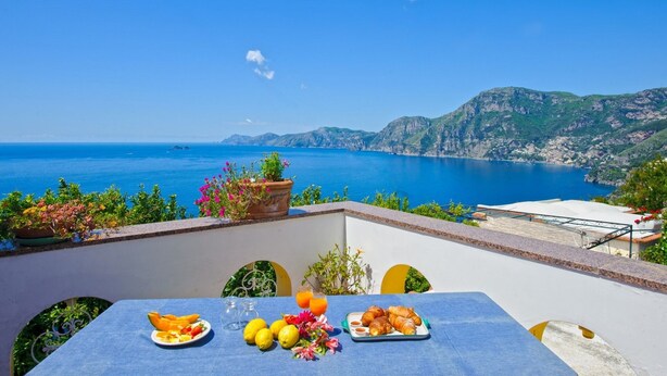 Une table dressée avec des aliments pour le petit-déjeuner, offrant une vue sur la mer et les montagnes.
