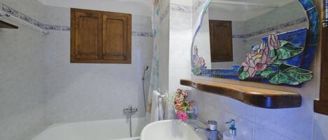 Une salle de bain avec une baignoire, un lavabo, un miroir orné de motifs floraux et un meuble en bois.