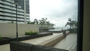 A modern outdoor area with a pool, palm trees, and a high-rise building in the background. - Torres Bellini II (Guayaquil)