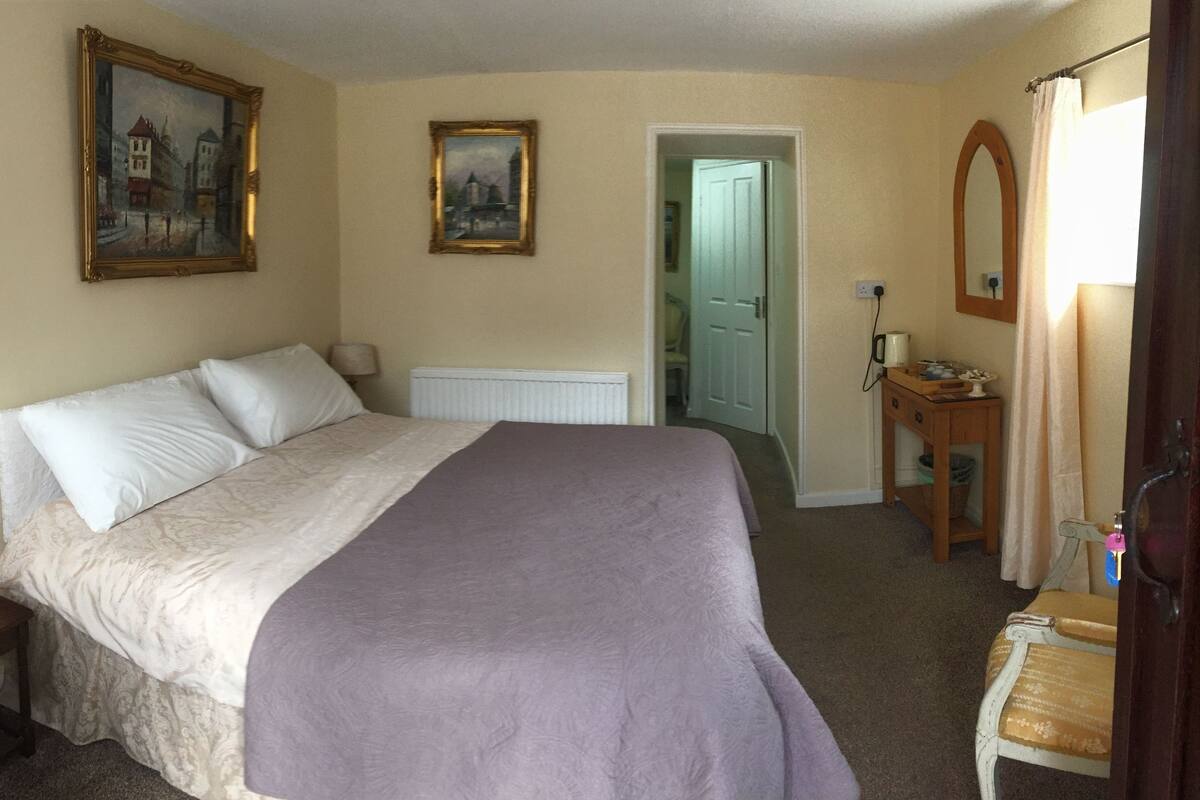 A bedroom with a bed, a nightstand, a dresser, a mirror, and two framed pictures on the wall.