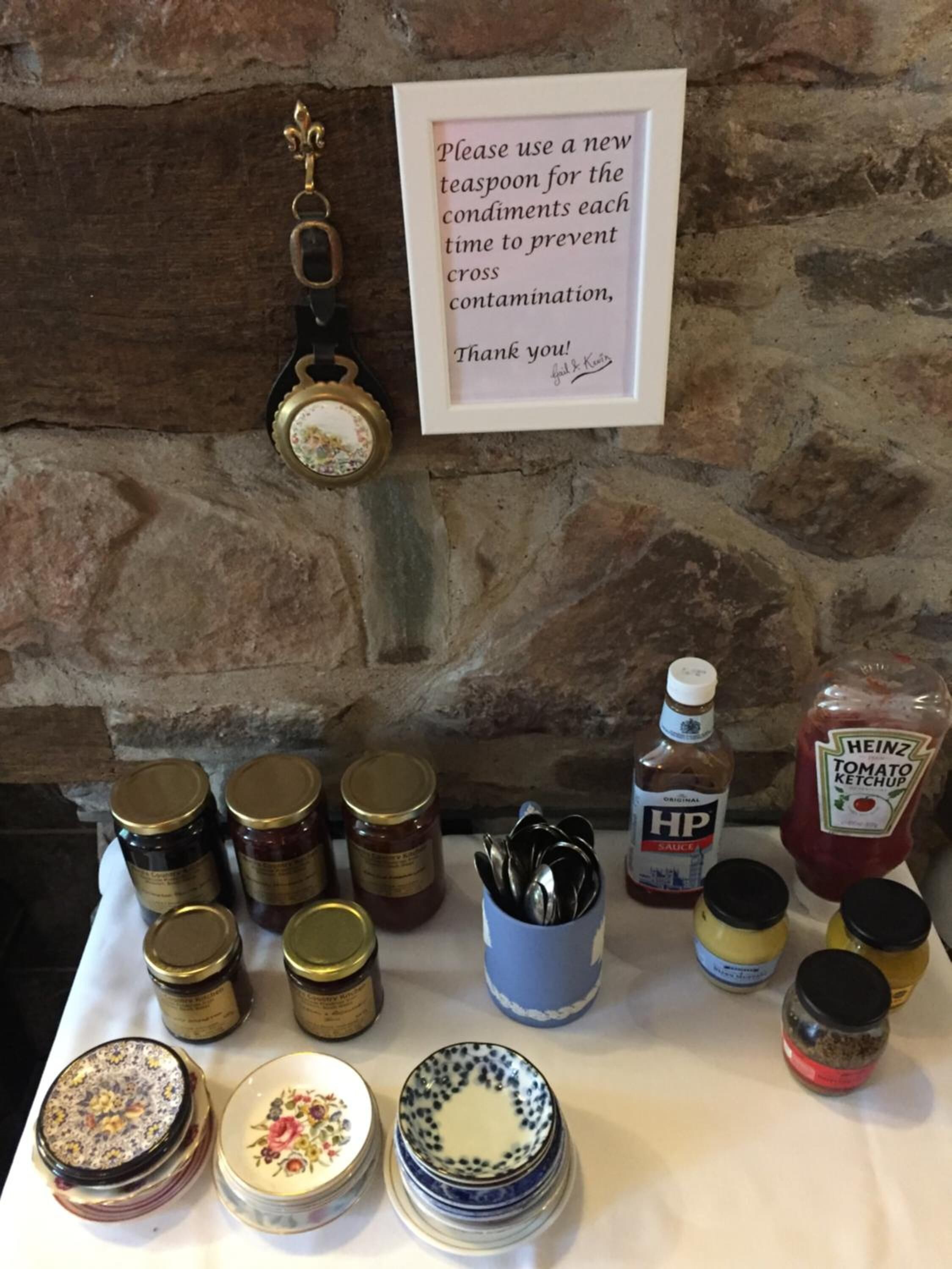 A table with condiments and a sign advising to use a new spoon for each condiment to prevent cross-contamination.