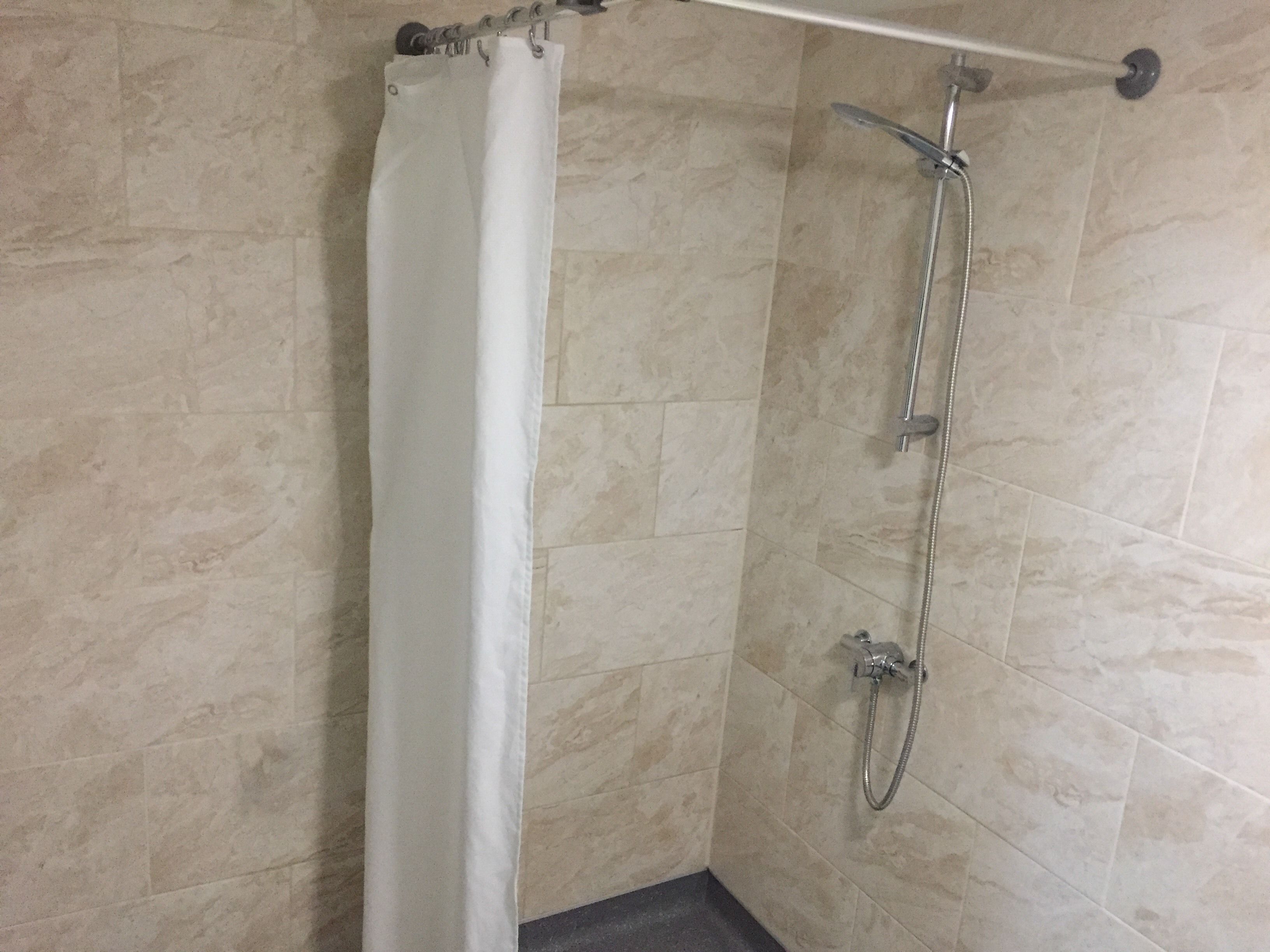A shower with a curtain, a handheld showerhead, and a wall-mounted faucet.