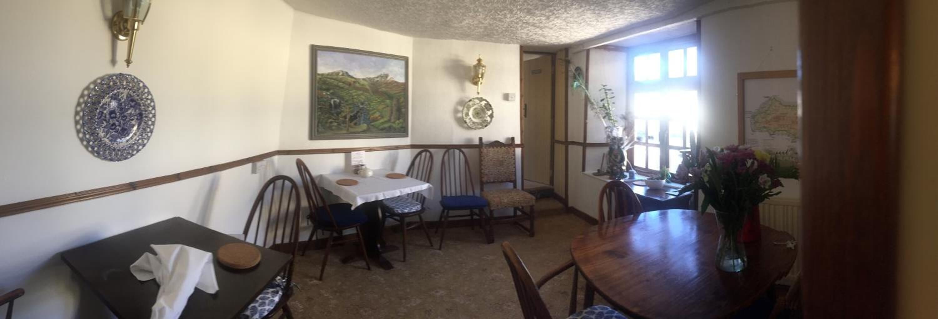 A dining area with a table and chairs, a decorative plate on the wall, and a window with a view of greenery.