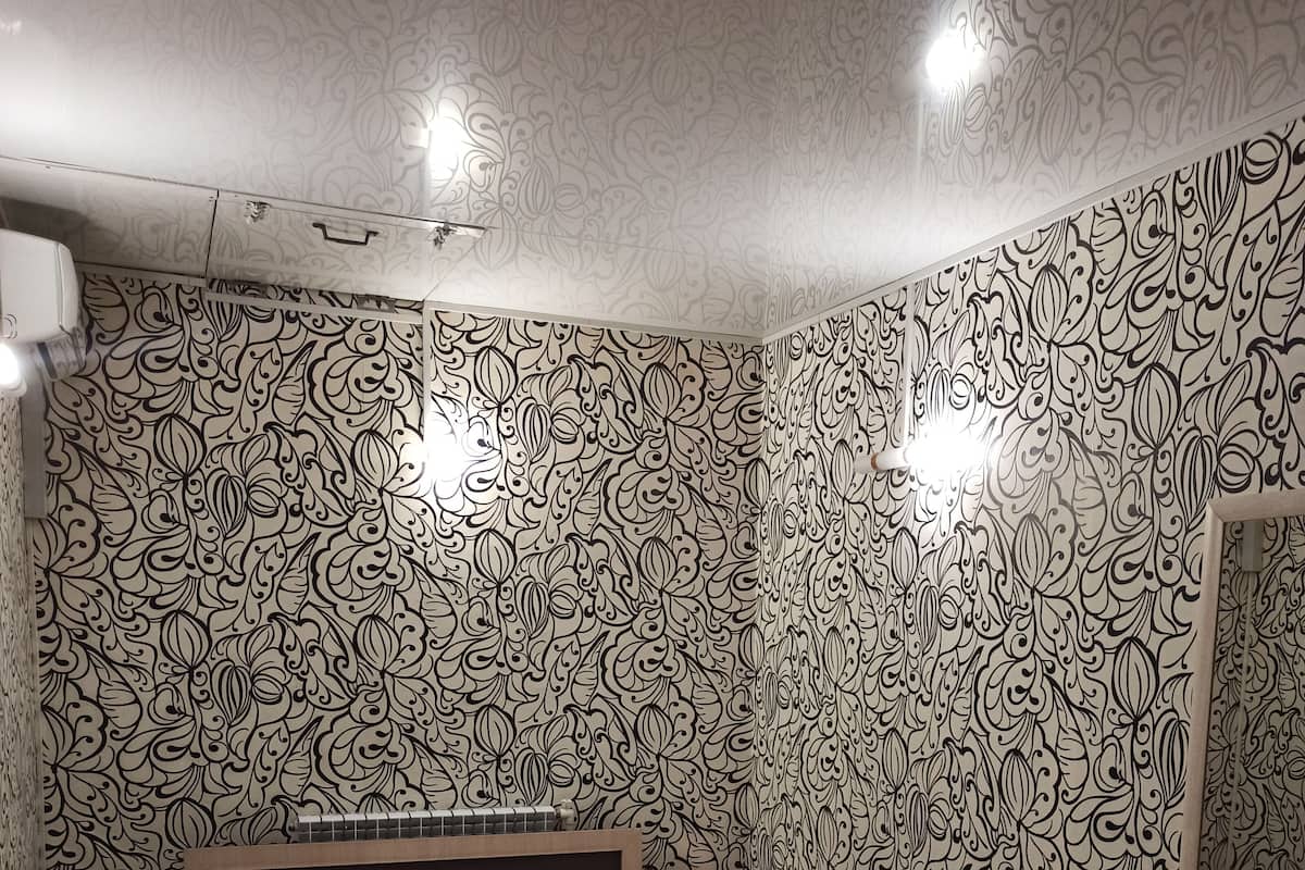 Ein Schlafzimmer mit gemustertem Wandpapier, einem Bett mit Blumenmuster auf der Tagesdecke, einem Nachttisch und einem Spiegel an der Wand.