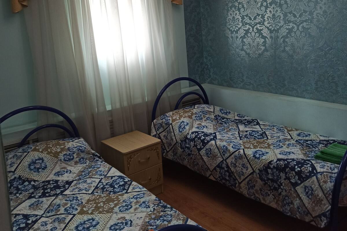 Ein Zimmer mit zwei Betten, einem kleinen Nachttisch, einem Deckenventilator und einer Wand mit Muster.
